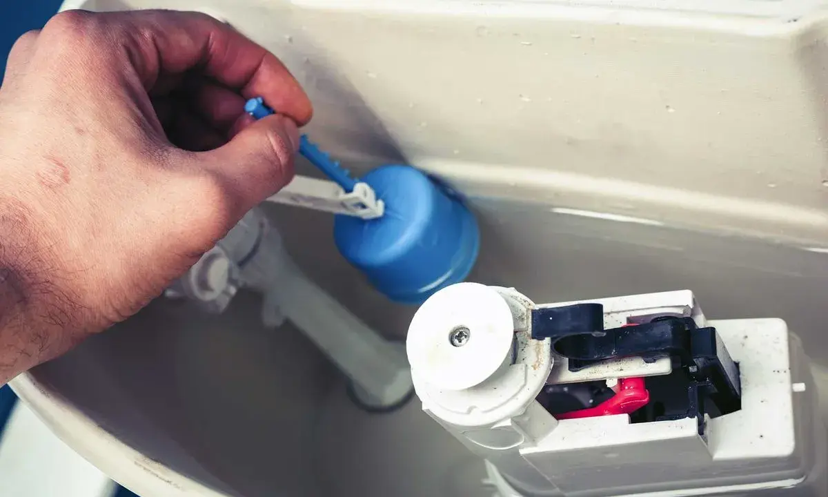 Mano ajusta el flotador azul de la cisterna, solucionando la fuga.