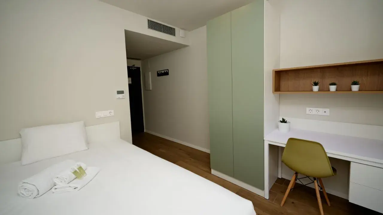 Habitación moderna con cama, armario verde y escritorio. Un espacio acogedor en Xior The Lofttown, listo para tu estancia.