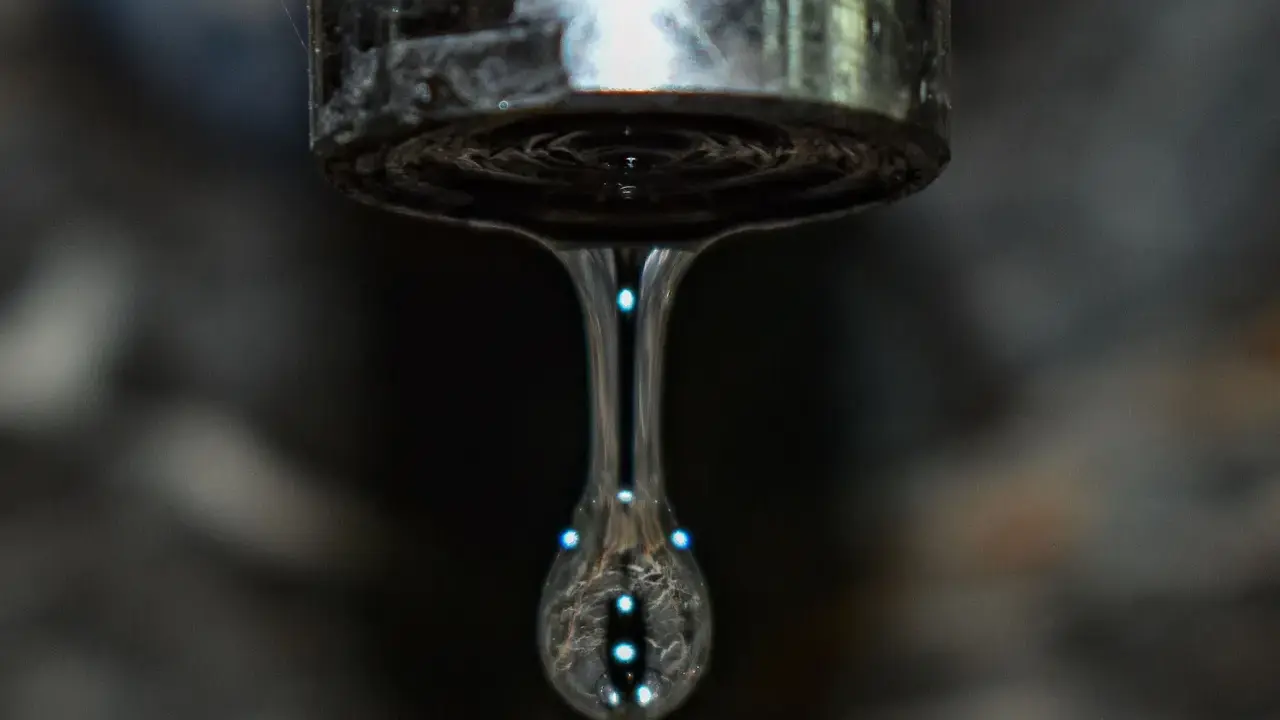 Un grifo que gotea, con una gota de agua capturada en el aire, reflejando luces como pequeñas estrellas.