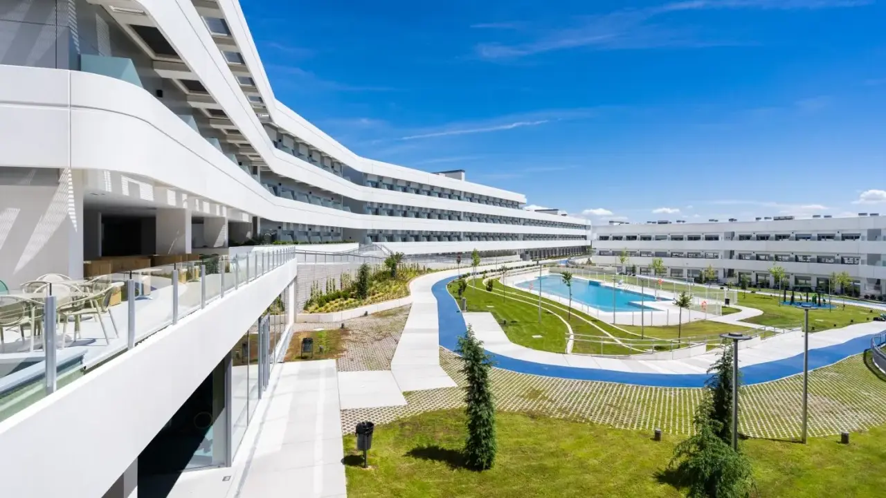 Modern residence in Madrid with curved white buildings, a pool, and green spaces.