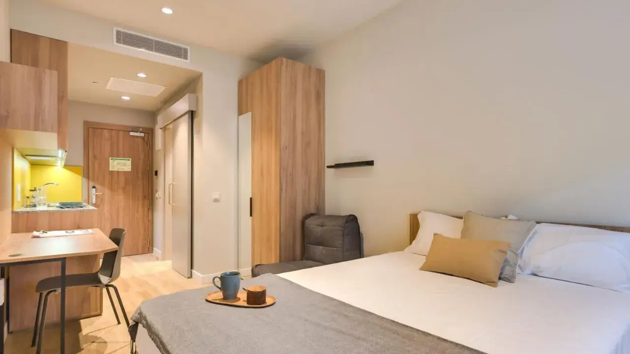 Habitación moderna con cama, escritorio y cocina. Descubre los livensa living precios para tu estancia.