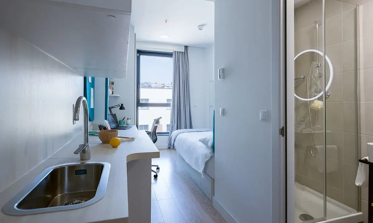 Cocina y baño moderno en residencia Garbi. Habitación con cama, escritorio y ventana.