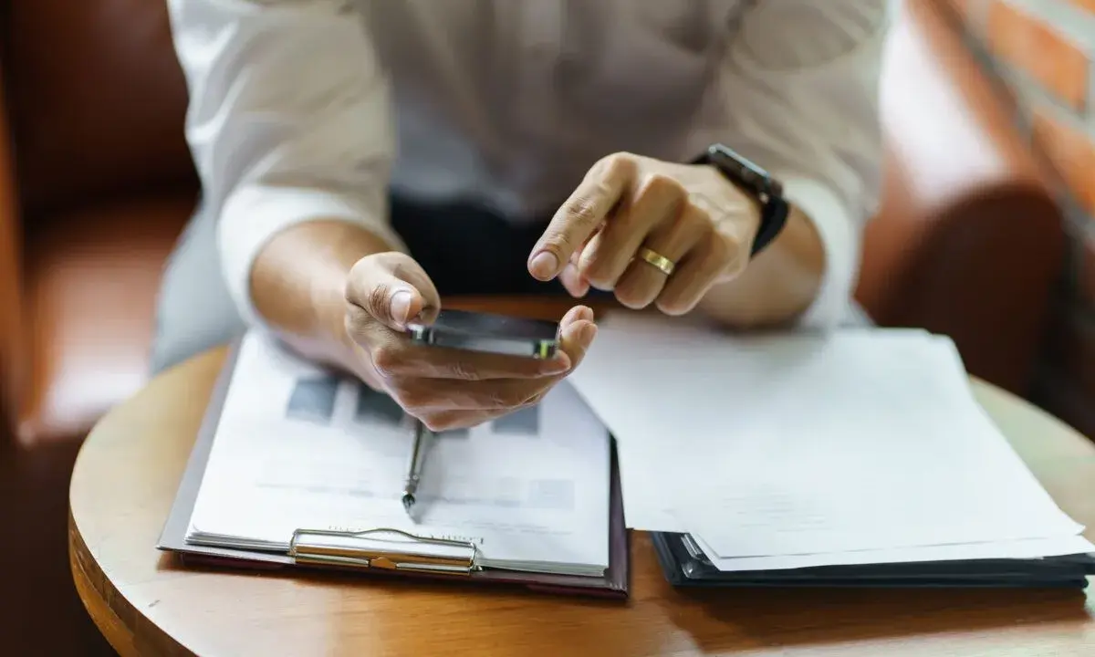 Hombre revisa su móvil, con documentos de modelo fin de contrato de alquiler y entrega de llaves sobre la mesa.