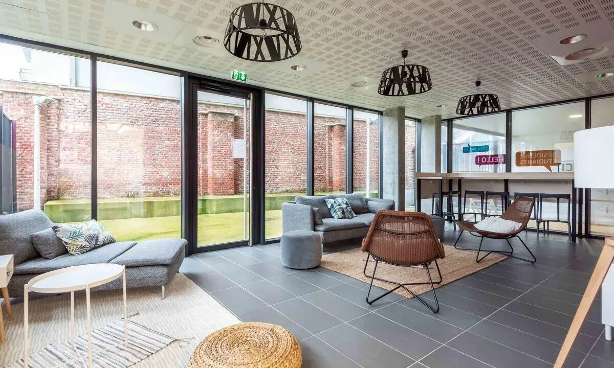 Espacio moderno con sofás grises, sillas de mimbre y mesa alta. Ideal para studea novalille, con grandes ventanales y ladrillos a la vista.