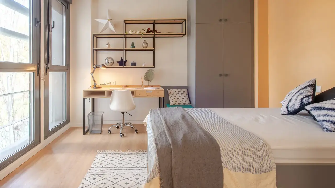 Habitación moderna en residencia San Bernardo Madrid. Escritorio, cama y armario gris. Ventanal con luz natural.
