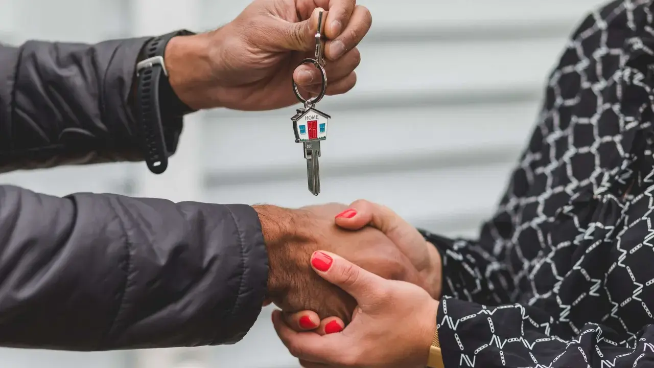 Man entrega llave de casa con llavero de hogar, mientras estrecha la mano de una mujer. Un símbolo de esperanza y fin de la suspensión de desahucios.