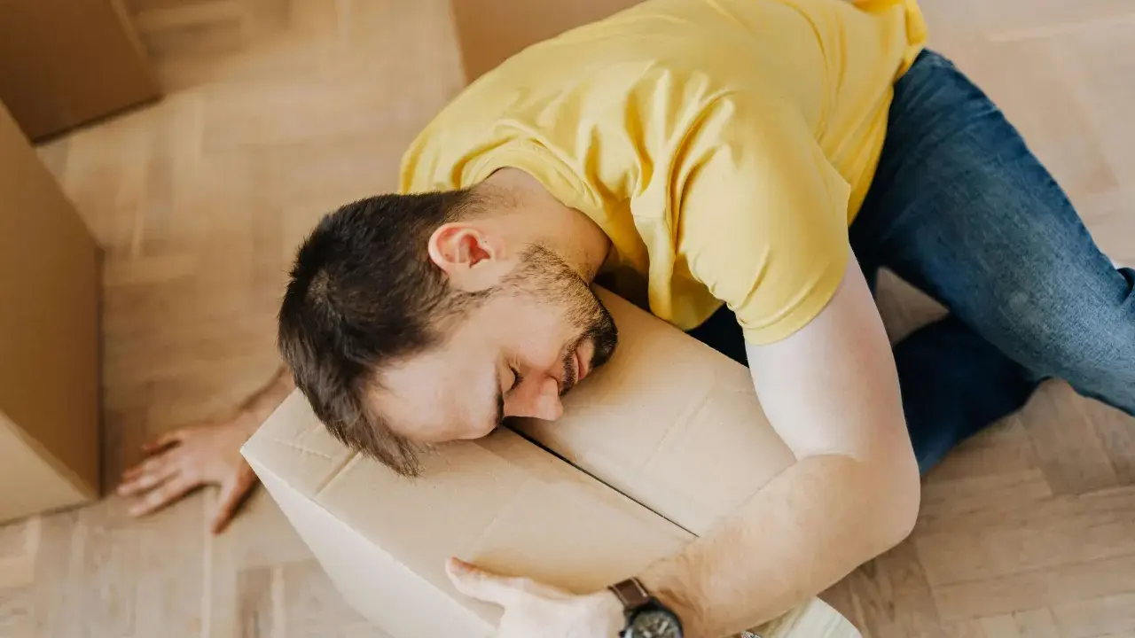 Hombre agotado durmiendo sobre una caja, quizás reflexionando sobre la diferencia entre comodato y precario tras una mudanza.