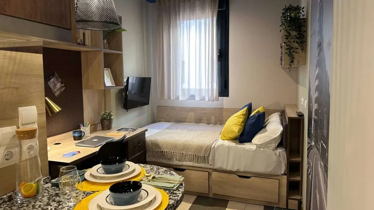 Estudio moderno en Livensa Living Madrid Aravaca con cama, escritorio, TV y mesa.