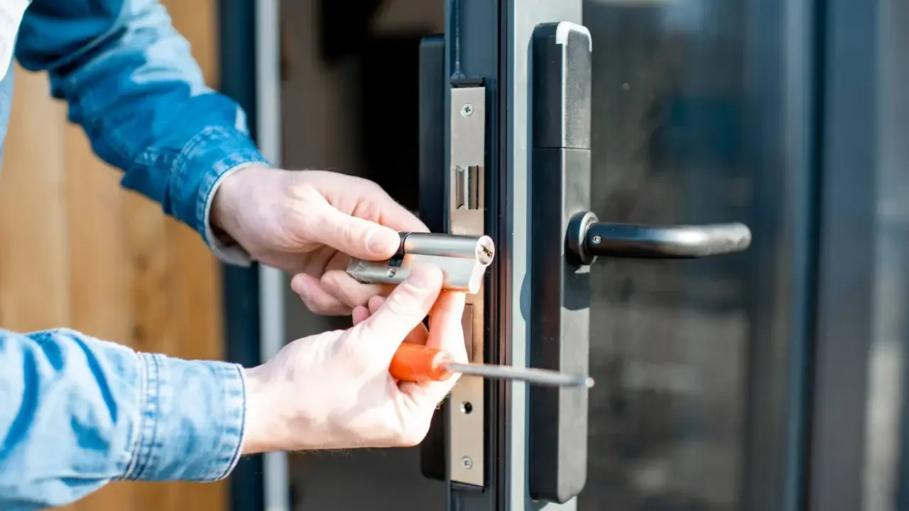 Man con camisa de mezclilla instala un cilindro de cerradura en una puerta, resolviendo un problema de comodato precario.