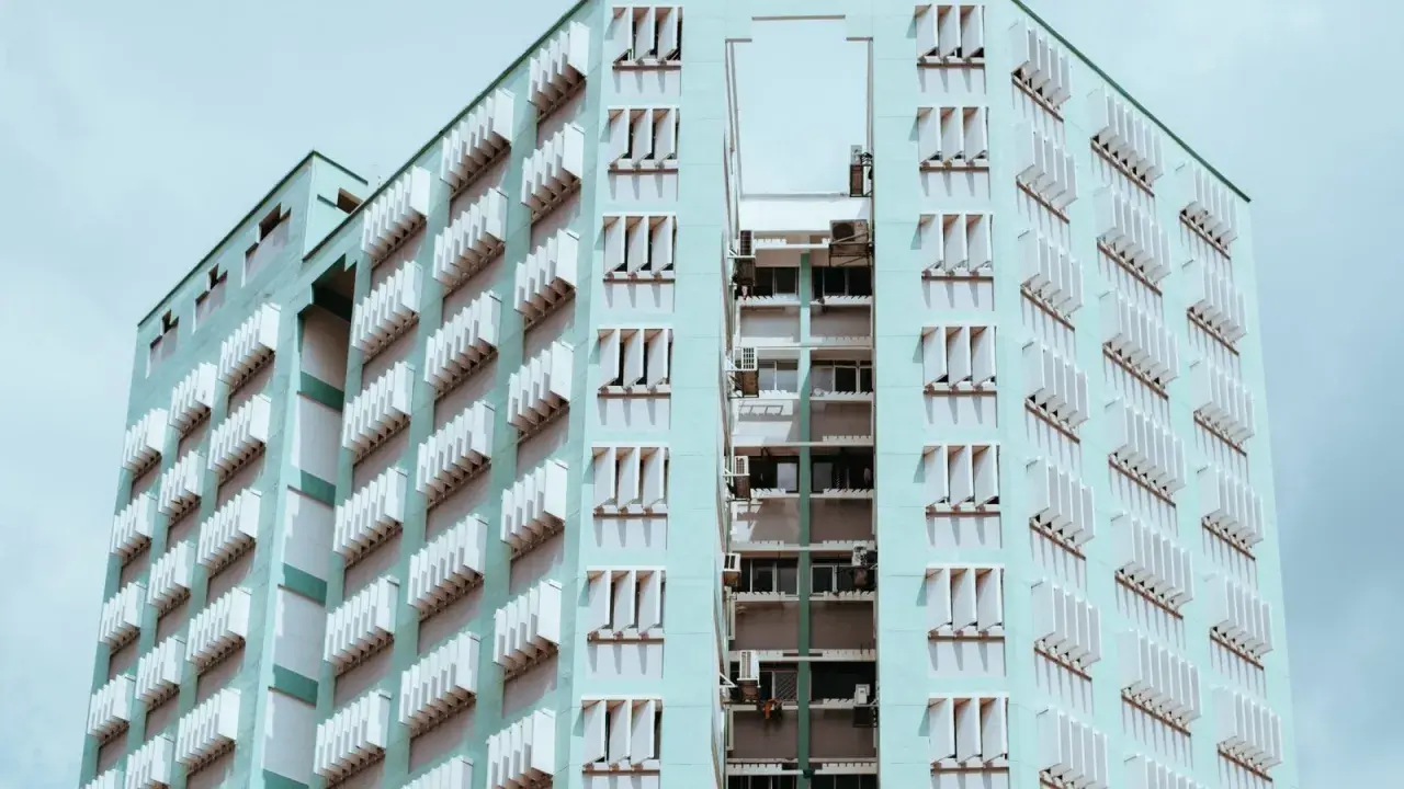 Edificio de apartamentos de color menta con filas de ventanas y persianas blancas. Un recordatorio de que se puede echar a un inquilino por necesitar el piso.