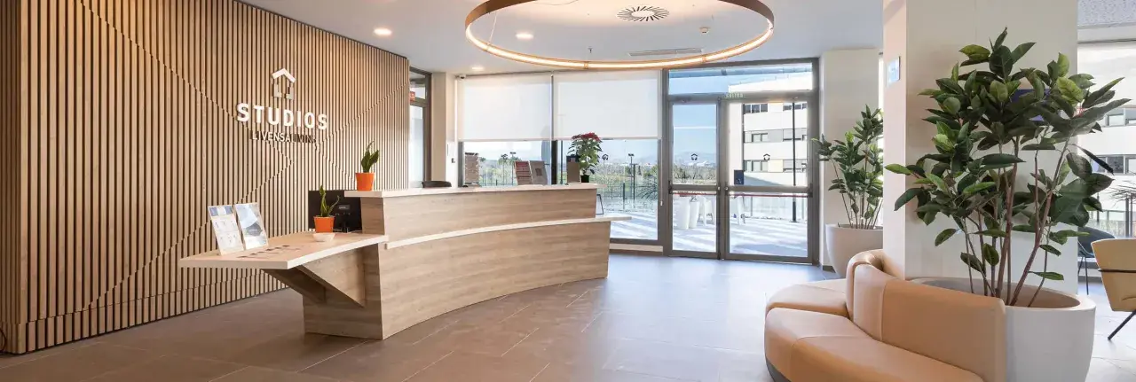 Recepción moderna y luminosa de living studios Alcobendas, con mostrador curvo, plantas y un sofá curvo.