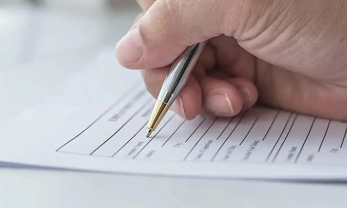Mano firmando un contrato de arrendamiento con bolígrafo plateado y dorado.