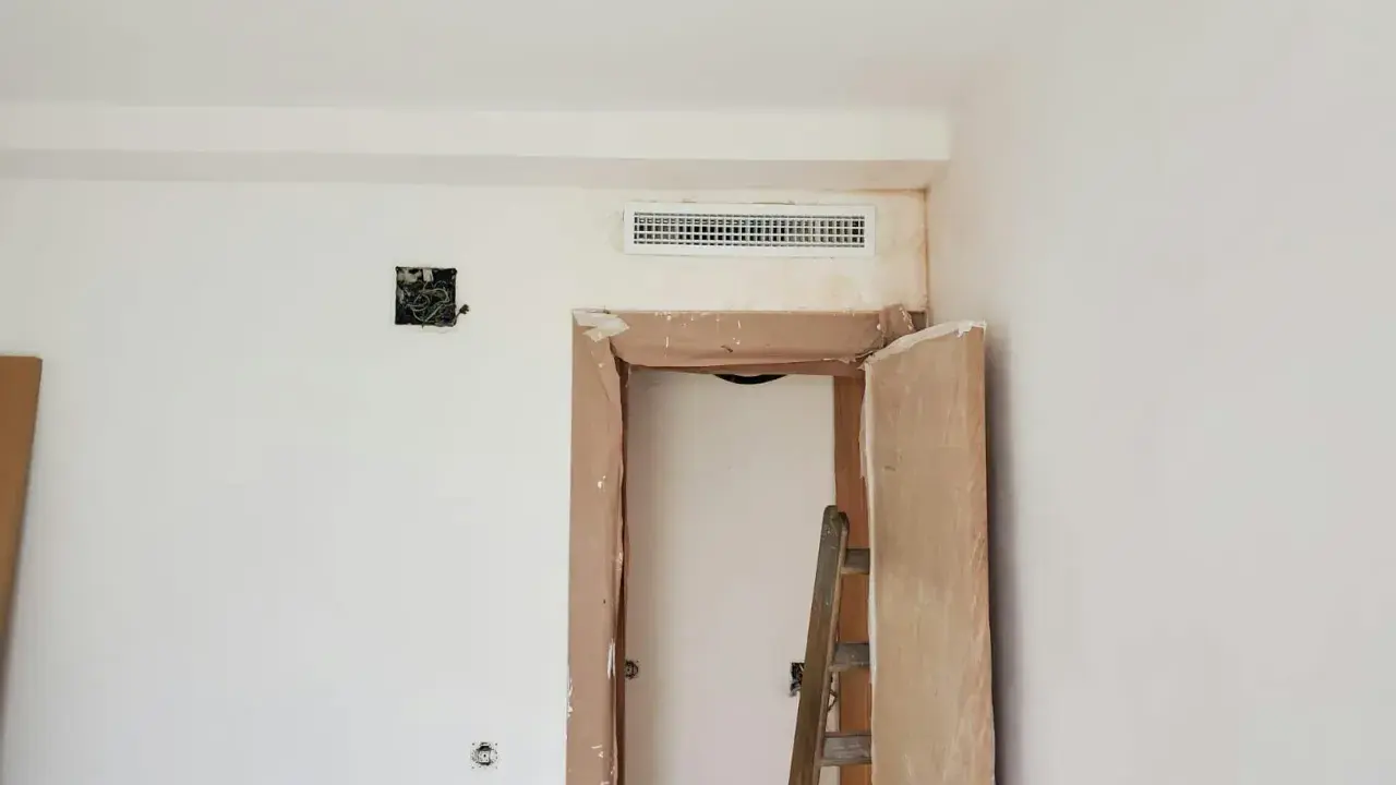 Habitación en obra con rejilla de preinstalación aire acondicionado en la parte superior de la puerta. Escalera y materiales de construcción.