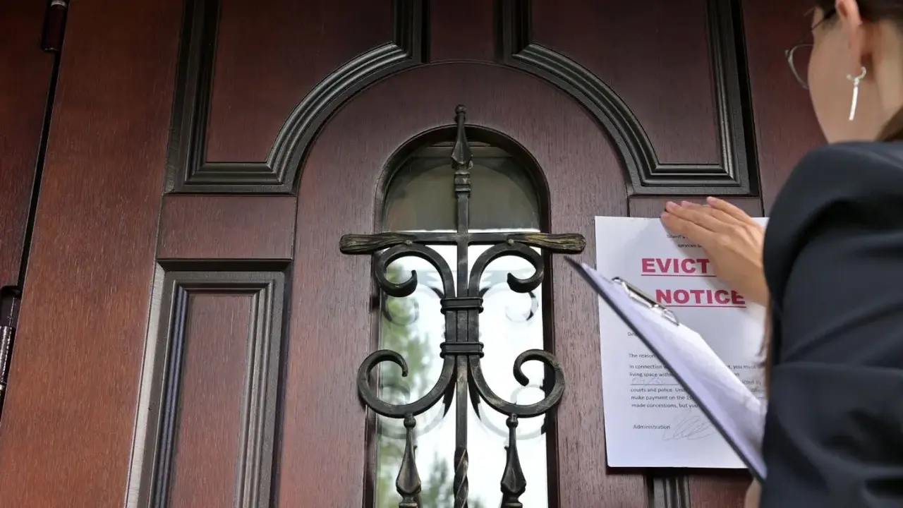 Mujer coloca un aviso de desalojo en una puerta de madera. Proceso para como echar a un inquilino sin contrato.