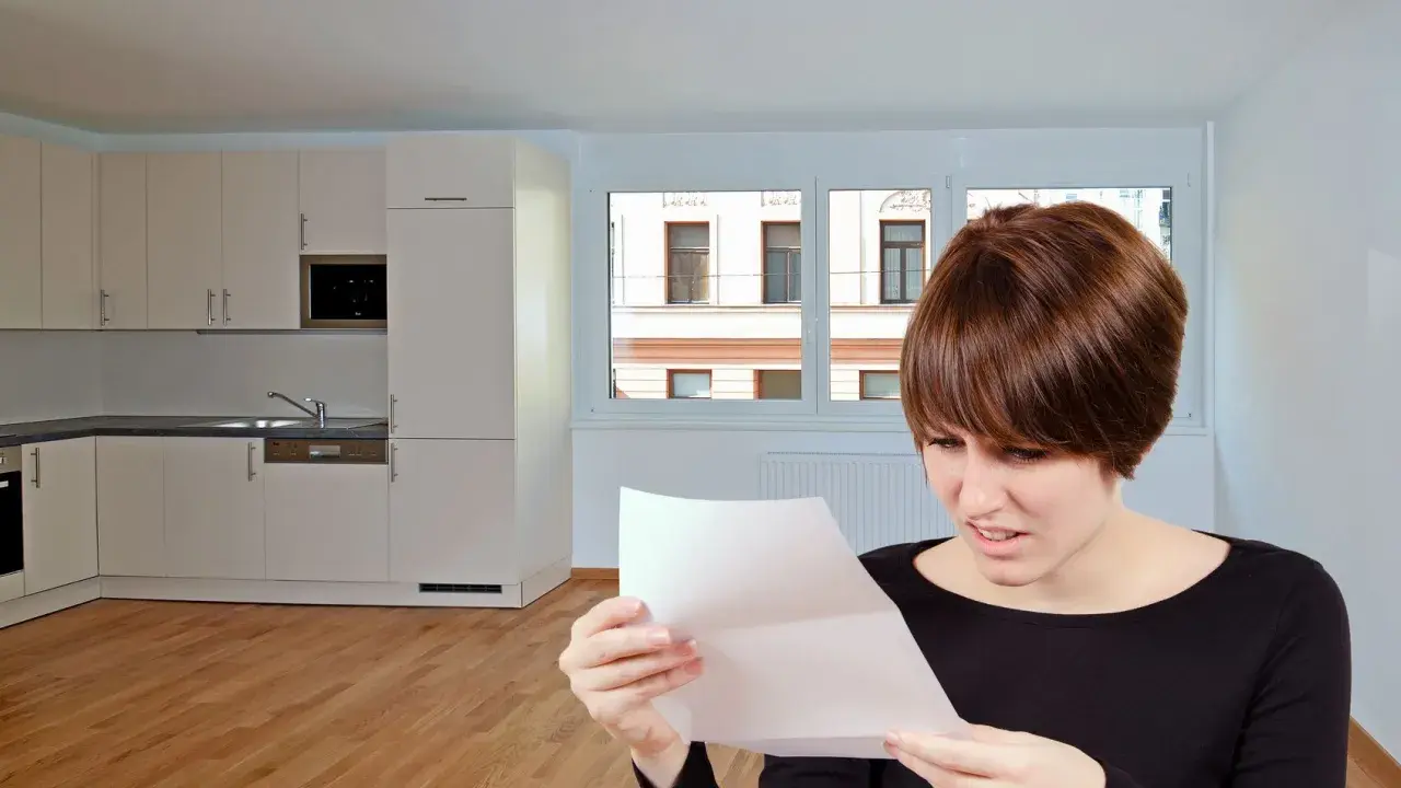 Mujer preocupada lee carta en cocina vacía. Podría ser una comunicación sobre la rescisión del contrato de alquiler.