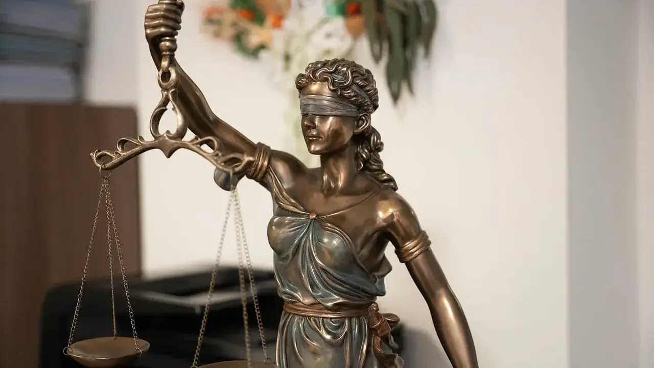 Estatua de la Justicia con venda y balanza, símbolo de imparcialidad. El texto "250.2 lec." aparece sutilmente.
