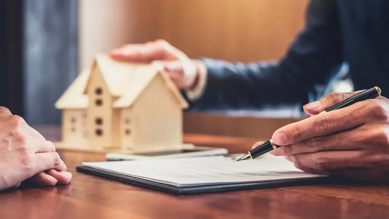 Firma de contrato de alquiler, con una maqueta de casa y un bolígrafo. Podría ser el inicio de un desahucio por precario si no se cumplen los términos.