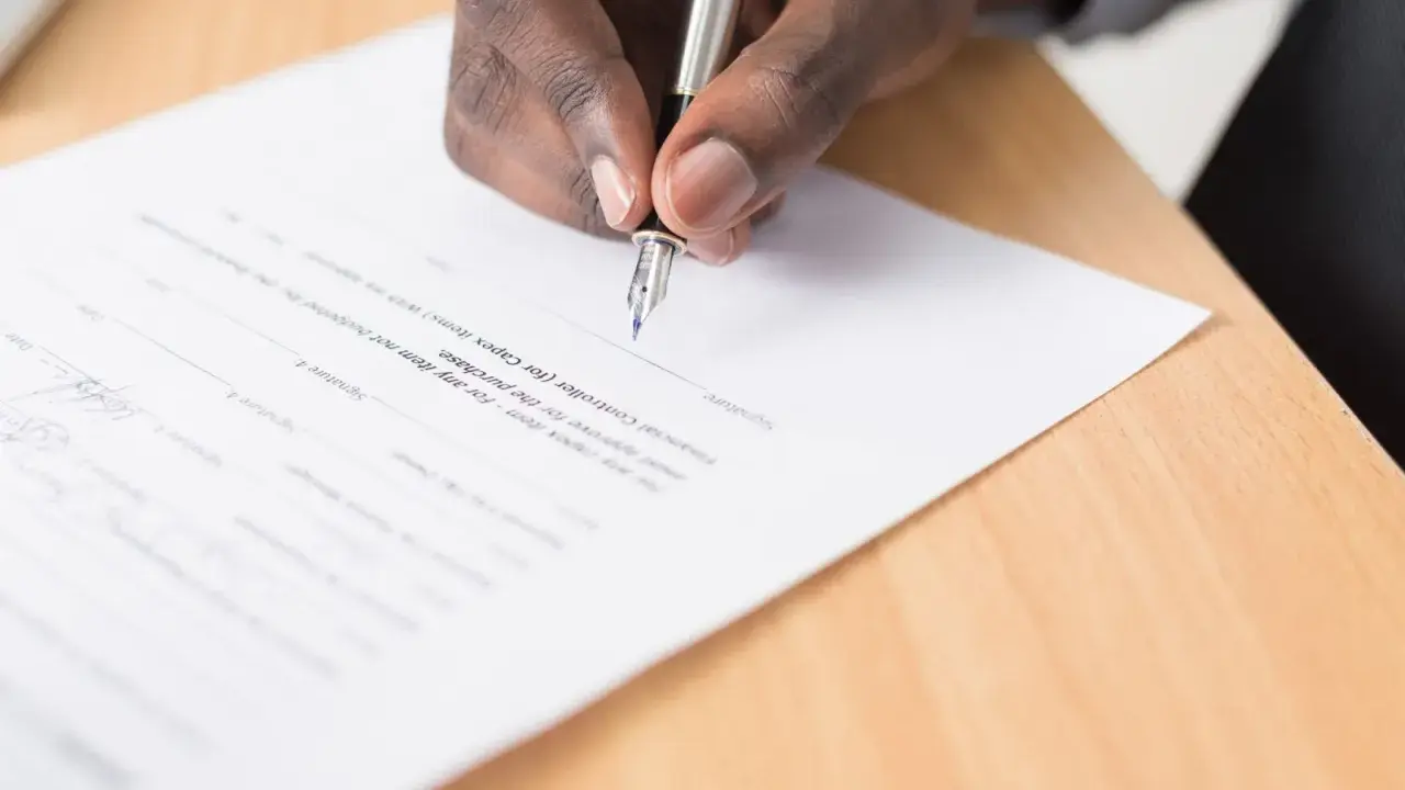 Mano firmando un documento, cumpliendo con el artículo 6 de la LAU, que requiere aprobación para la compra.