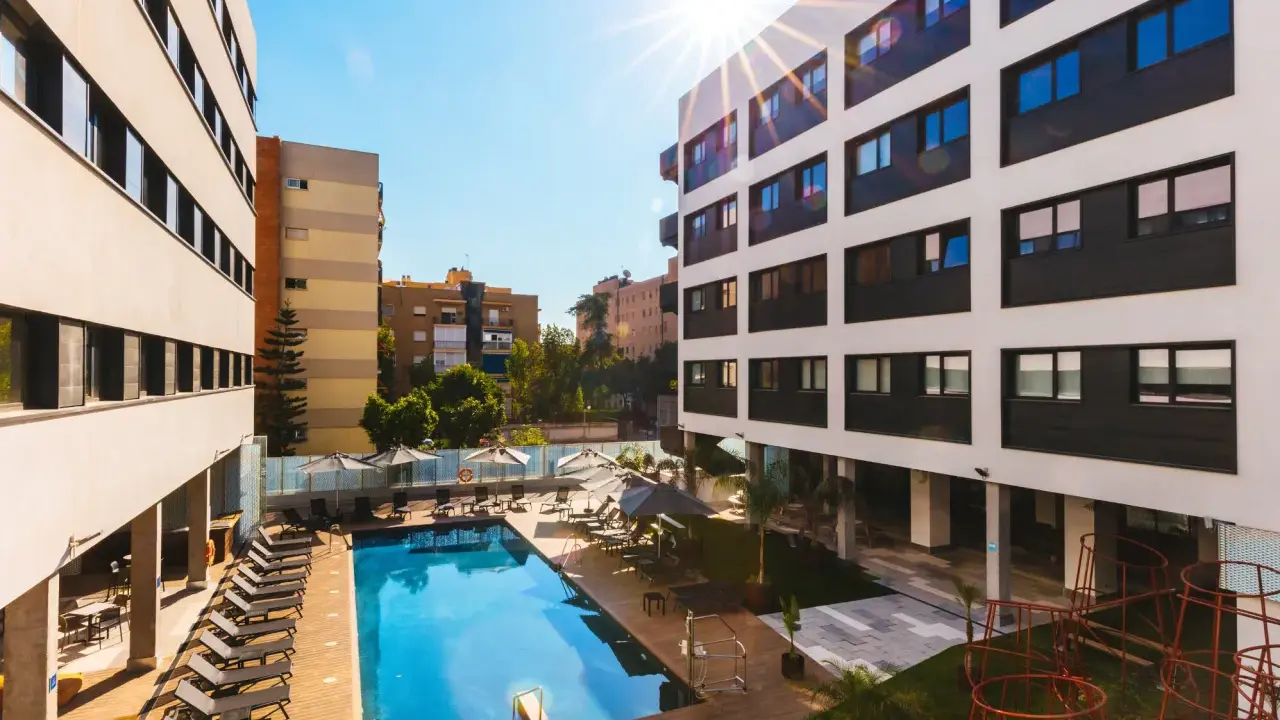 La residencia de estudiantes Livensa Living Sevilla luce su piscina y zonas comunes bajo el sol.