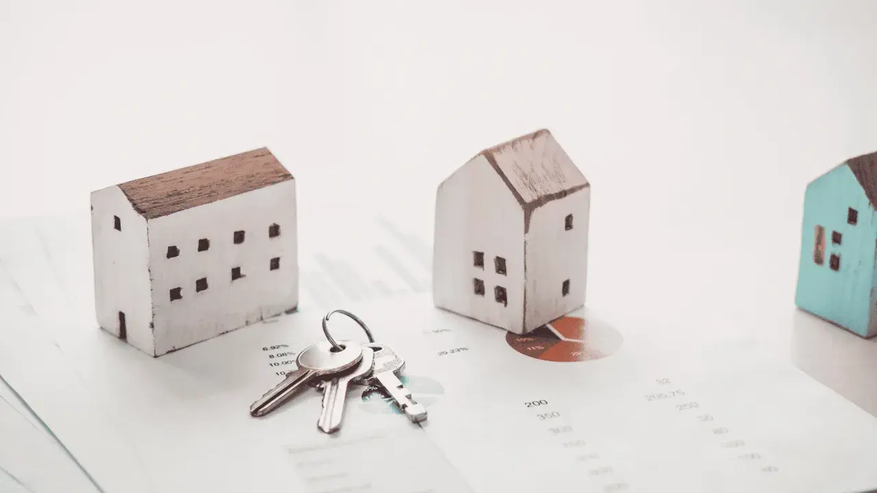 Maquetas de casas y llaves sobre gráficos financieros. El arte 17 lau sugiere una inversión inmobiliaria.