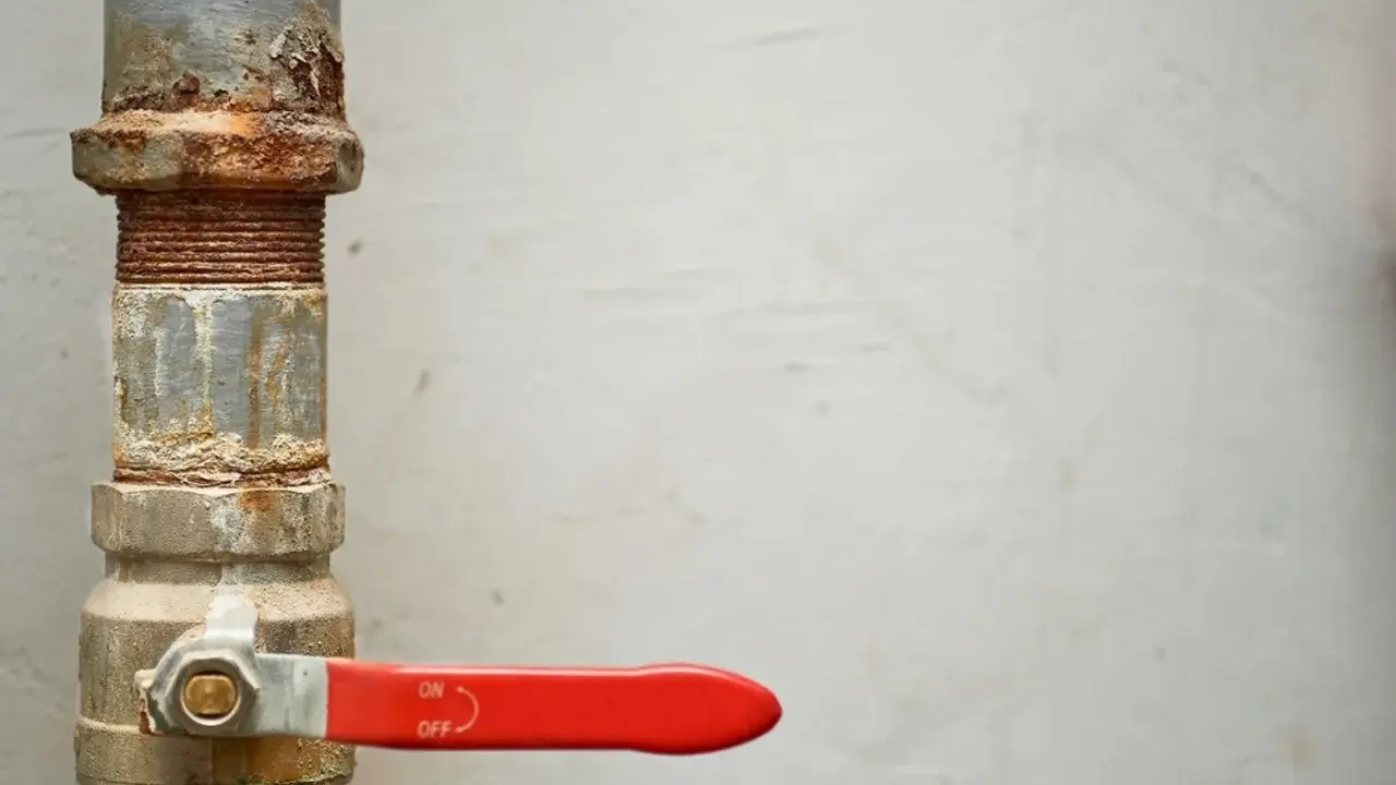 Llave de paso agua antigua, oxidada y con palanca roja, controlando el flujo.
