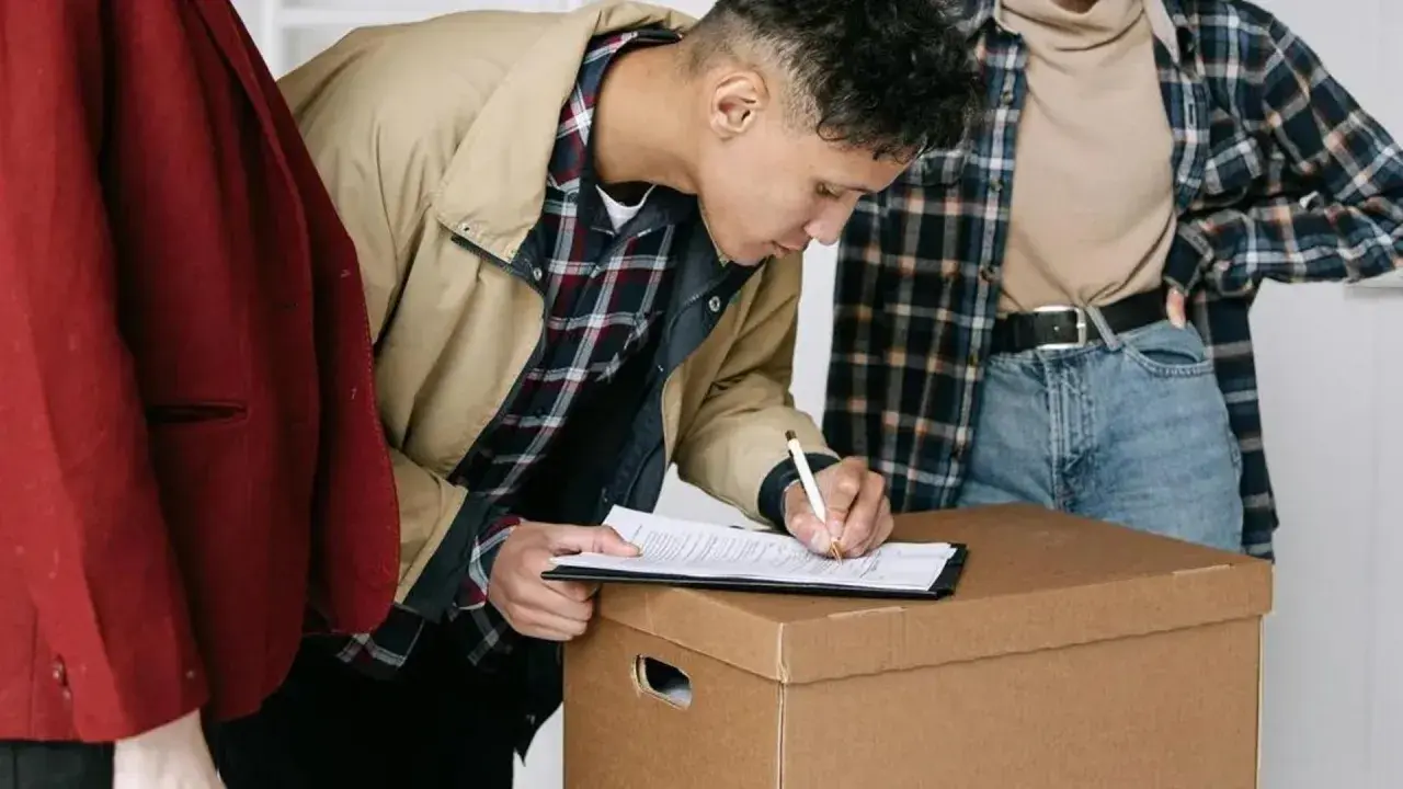 Joven firma contrato de arrendamiento de vivienda, rodeado de cajas.