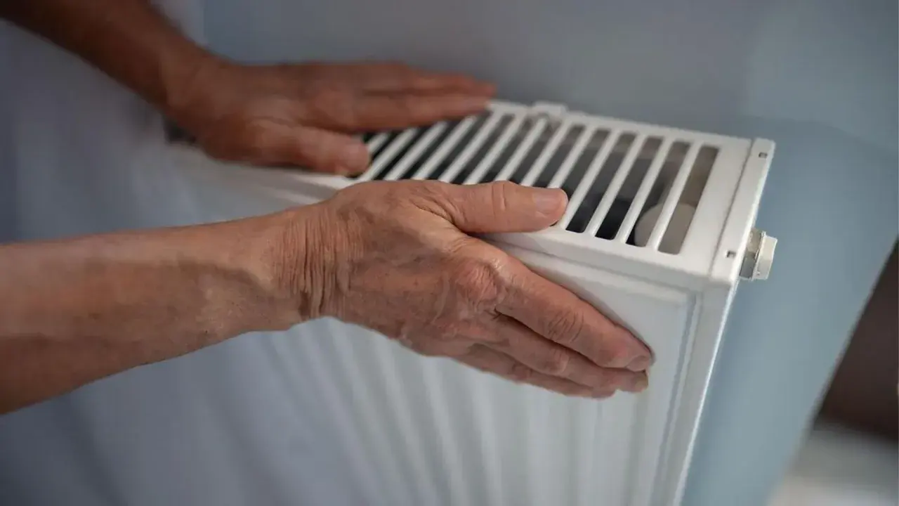 Manos sobre un radiador blanco, sintiendo el calor. Quizás se pregunte porque suenan los radiadores.