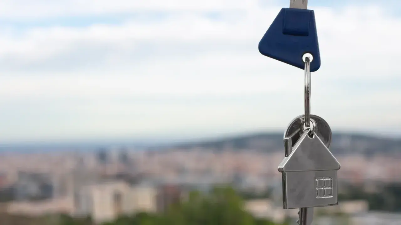Llaves con un llavero en forma de casa, simbolizando un contrato de opción de compra. Fondo de ciudad difuminado.