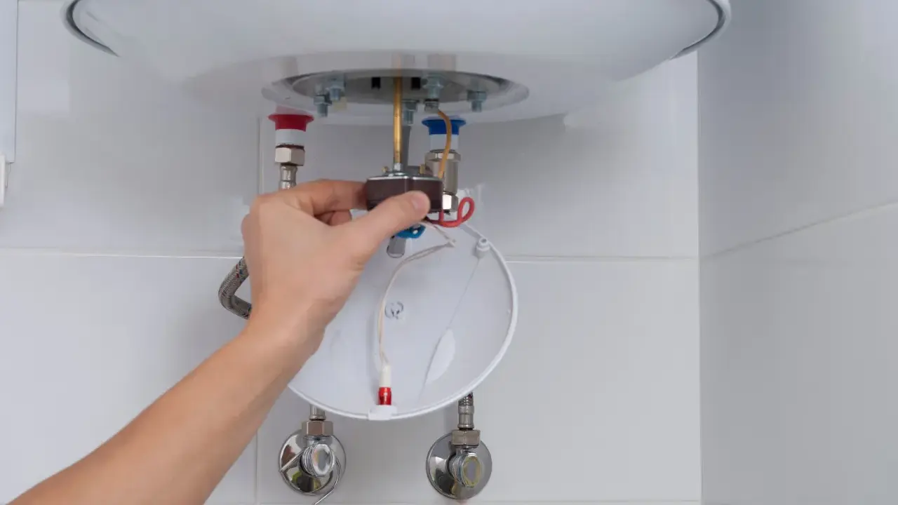 Mano ajustando el termostato de un calentador de agua, parte del proceso para saber como limpiar un termo por dentro.