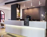 Recepción moderna y luminosa de la residencia Nuevo Versalles, con mostrador blanco, pantalla y máquina de efectivo.