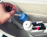 Mano ajusta el flotador azul de la cisterna, solucionando la fuga.