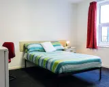 Habitación en Atlantic Point, Liverpool, con cama a rayas verdes y azules, escritorio rojo y ventana con cortina roja.
