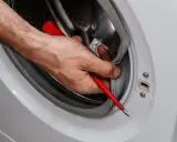 Mano con destornillador limpiando la goma de la lavadora. Aprende como quitar el moho de la goma de la lavadora para un mejor lavado.