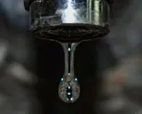 Un grifo que gotea, con una gota de agua capturada en el aire, reflejando luces como pequeñas estrellas.
