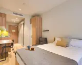 Habitación moderna con cama, escritorio y cocina. Descubre los livensa living precios para tu estancia.