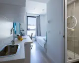 Cocina y baño moderno en residencia Garbi. Habitación con cama, escritorio y ventana.