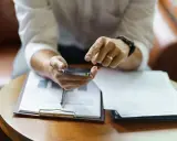 Hombre revisa su móvil, con documentos de modelo fin de contrato de alquiler y entrega de llaves sobre la mesa.