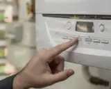 Dedo presionando botón en panel de caldera. Se observa pantalla digital y símbolos.