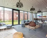 Espacio moderno con sofás grises, sillas de mimbre y mesa alta. Ideal para studea novalille, con grandes ventanales y ladrillos a la vista.