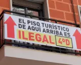 Cartel en balcón: "El piso turístico de aquí arriba es ilegal". Prohibición pisos turísticos.