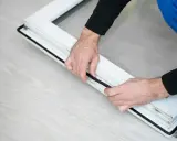 Manos colocando burletes en un marco de ventana blanco. Aprende como poner burletes en ventanas para mejorar el aislamiento.
