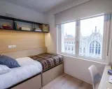 Habitación moderna con cama, estanterías y vistas a un edificio histórico en Xior Madrid Retiro.