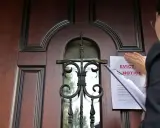 Mujer coloca un aviso de desalojo en una puerta de madera. Proceso para como echar a un inquilino sin contrato.