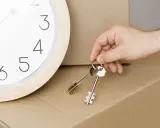 Un reloj marca el tiempo mientras una mano sostiene las llaves, simbolizando la inminencia de un contrato de alquiler temporal y una mudanza.