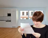 Mujer preocupada lee carta en cocina vacía. Podría ser una comunicación sobre la rescisión del contrato de alquiler.