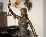 Estatua de la Justicia con venda y balanza, símbolo de imparcialidad. El texto "250.2 lec." aparece sutilmente.