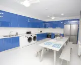 Cocina moderna con armarios azules brillantes, electrodomésticos y una mesa para compartir. Un espacio ideal para una **student factory** donde convivir y estudiar.