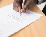 Mano firmando un documento, cumpliendo con el artículo 6 de la LAU, que requiere aprobación para la compra.
