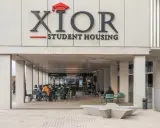 Estudiantes disfrutan en la **residencia Xior Picasso-Velázquez**. Un grupo toca música en vivo mientras otros charlan y comen al aire libre.