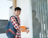 Estudiante sonriente con mochila y cuaderno, abriendo la puerta de las residencias CROUS París.